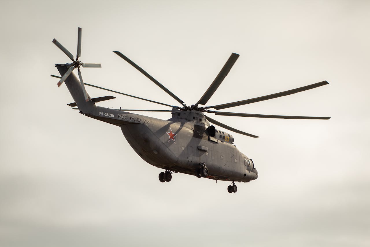 our-story-01 Low-angle view of a military helicopter in flight against a clear sky, showcasing its size and design.